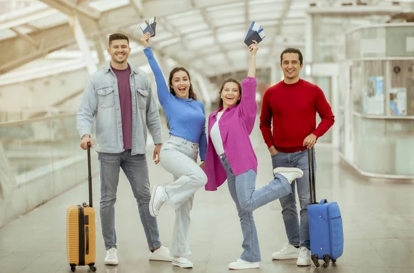 安いチケットを提供します 2組の友人が休暇中に搭乗券を保持し 空港内で一緒にポーズをカメラに笑顔旅行スーツケースと立っています — ストック写真