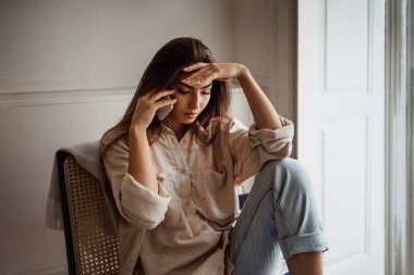 Mutsuz üzgün, ümitsiz, Asyalı genç bir kadın telefonla arıyor, konuşuyor, odada tek başına koltukta oturuyor. Kötü haber ve stres, baskı, dedikodu ve evde olumsuz tepkiler