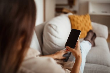 Genç Asyalı bir kadın akıllı telefonda boş ekranla yazı yazıyor, sosyal ağda sohbet ediyor, internette sörf yapıyor, odanın içindeki koltukta tanınmaz halde oturuyor. Uygulama, web sitesi, evde çevrimiçi blog