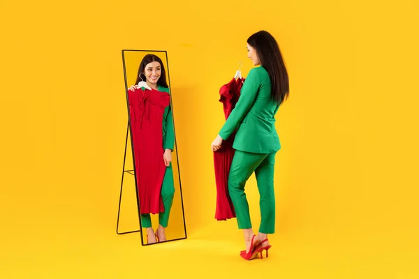 Šťastná Evropanka Držící Červené Šaty Dívající Svůj Odraz Zrcadle Zkoušející — Stock fotografie