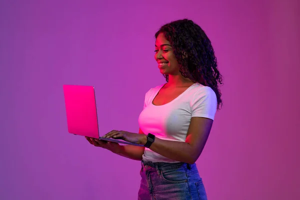 Gülümseyen Siyah Kadın Mor Arkaplanda Neon Işığı Altındayken Dizüstü Bilgisayar — Stok fotoğraf