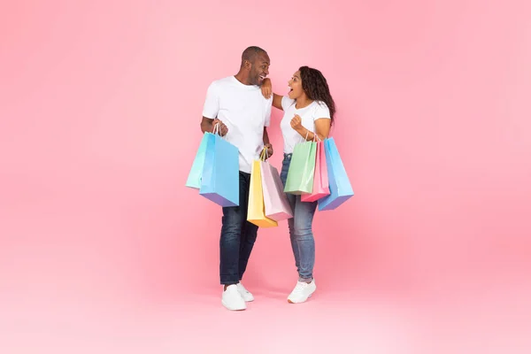 ファミリーショッピングのコンセプト 大きな販売の間にカラフルな買い物袋を持っている喜びの黒いカップルは ピンクの背景 フル長さ フリースペースの上にポーズ — ストック写真