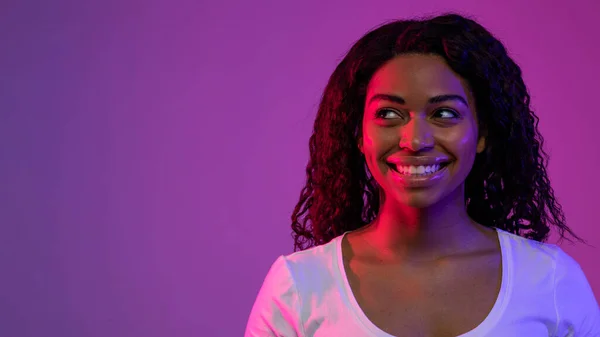 多愁善感的年轻黑人女性站在紫色背景 复制空间的霓虹灯下 饶有兴致地凝视着远方 梦想着非洲裔美国女性的画像 — 图库照片