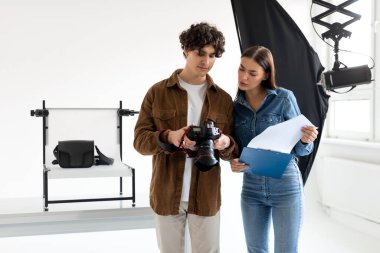 Profesyonel fotoğrafçının genç bayan asistanı elinde video veya fotoğraf çekiminin detaylarını tartışıyor, fotostudin içinde duruyor ve fotoshoot için hazırlanıyor.