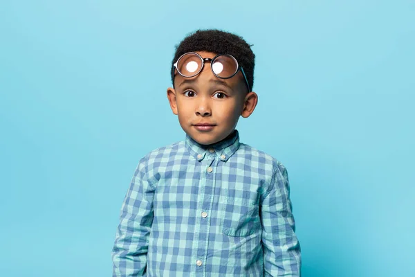 孩子和视力问题 非裔美国男孩摘下额头上的眼镜 看着镜头 站在蓝色的背景上 有视力问题的可爱的黑人男孩 — 图库照片