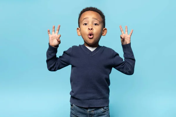 兴奋的黑人男孩用双手摆出一副不错的姿势 用惊讶的表情看着镜头 站在蓝色的背景上 男孩儿用手指做同意标志 — 图库照片