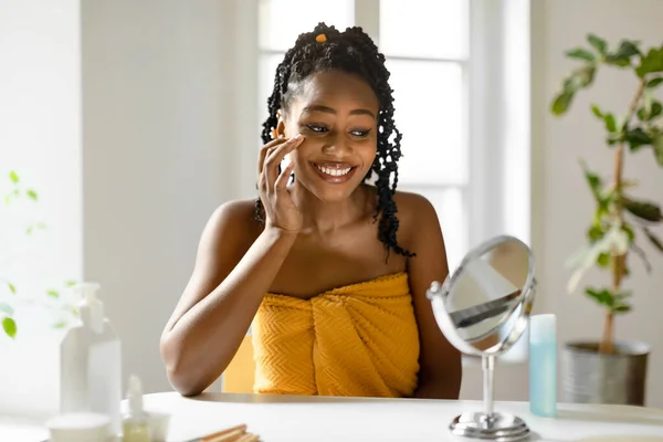 鏡を見ながらアイクリームを塗ったり タオルで包んだり 自宅で美容トリートメントをしたり セルフケア フリースペースを楽しんでいる幸せなアフリカ系アメリカ人女性 — ストック写真
