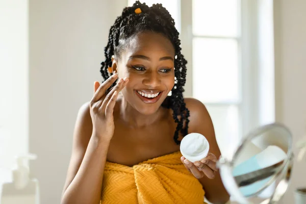 毎日の美しさルーチン 幸せな黒の女性が顔に保湿クリームを適用し 栄養肌と笑顔を使用して 寝室の拡大鏡を見て 無料のスペース — ストック写真
