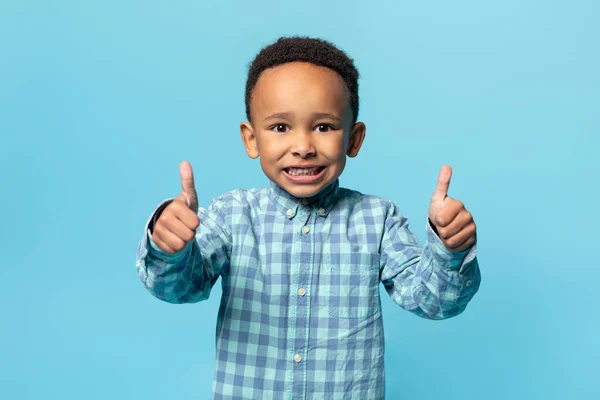 我喜欢它 快乐的非洲裔美国可爱的男孩竖起大拇指 面带微笑 在蓝色的工作室墙壁背景上摆出孤立的姿势 复制空间 — 图库照片