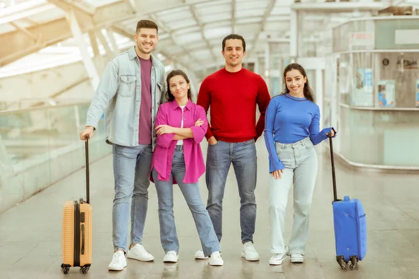 友達と旅行する 現代の空港の屋内でスーツケースと一緒に休暇に行く2人のカップル カメラに微笑む 幸せな観光客のグループターミナルでポーズ 観光コンセプト — ストック写真