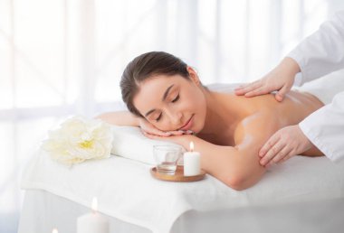 Güzel Hintli kadın spa merkezinde rahatlatıcı aromaterapi masajı yaptırıyor, sakin çekici bir kadın çiçek ve yanan bir mumla masada uzanıyor, sağlık ve güzellik tedavilerinin tadını çıkarıyor.