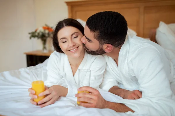 Loving Couple Kissing Drinkend Sinaasappelsap Liggend Bed Hotelkamer Binnen Echtgenoten — Stockfoto