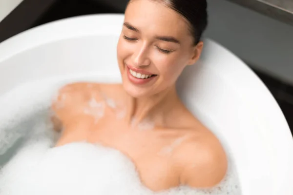 自宅の浴室で目を閉じて泡リラックスしてお風呂に入る陽気な女性 温泉の日を楽しむ若い白人女性の入浴のショットの上のビュー — ストック写真
