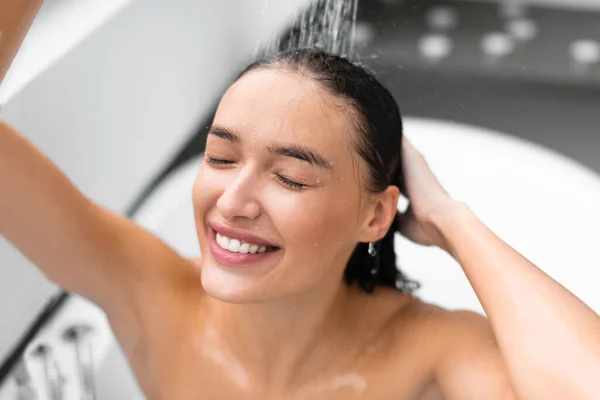 現代の浴室の屋内でリラックスした水の下でさわやかなシャワーを浴び頭と体を閉じる目を取り美少女 選択的フォーカス ウェルネス スパコンセプト — ストック写真