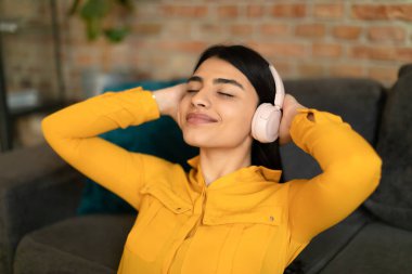 Kablosuz kulaklıkla müzik dinleyen mutlu Meksikalı genç bayan elleri başının arkasında ve gözleri kapalı dinleniyor. Teknoloji ve rahatlama kavramı