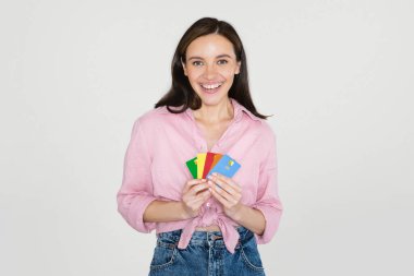 Havalı, güler yüzlü, günlük kıyafetlerle gülümseyen genç bir bayan ellerinde banka kartlarıyla, gri stüdyo geçmişine bakıyor. Temassız ödeme, modern bankacılık kavramı