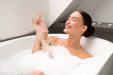 Mutlu bir kadın banyo yaparken, gözleri köpükle kapalıyken ve evdeki modern banyoda ellerini yıkarken mutlu olur. Güzellik Günü 'nde yıkanan kadınlar. Spa ve Şımartma Konsepti