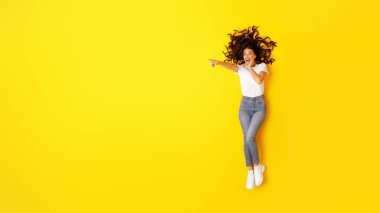 Stüdyodaki sarı arka planda yalan söyleyen heyecanlı bayan, mesaj atmak için boş uzayı işaret ediyor. Konsepte bir bak. Panorama, Görünümün Üstü