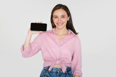 Modern cep telefonunu siyah ekranda gösteren, gülümseyen, güzel mobil uygulama gösteren ya da harika bir teklif sunan, gri arkaplan, model model...