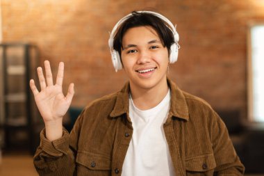 Neşeli Japon öğrenci, kulaklık takmış, el sallayarak sizi selamlıyor. Kameraya Gülümseyen Çocuk Hareketi. Eğitim Podcast Reklam Kavramı