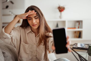 Üzücü, güzel, bin yıllık melez bir ırk kadını boş ekranlı akıllı telefon gösteriyor. Stres altında, oturma odasında depresyon yaşıyor. Sohbet için uygulama, kötü haber, evde eleştiriler