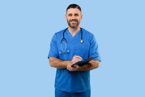 中年男性医師で制服作業で患者Anamnesis 立って上の青スタジオ背景と笑顔でカメラ フリースペース — ストック写真