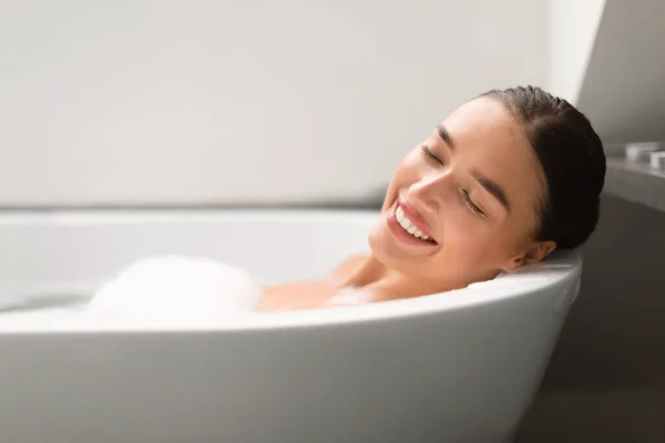 自宅のモダンなバスルームでリラックスしたバスタブに横たわっ泡でお風呂に入る女性のサイドビュー 目を閉じてポーズ リラクゼーション 入浴ルーティンのコンセプト 選択的フォーカス — ストック写真