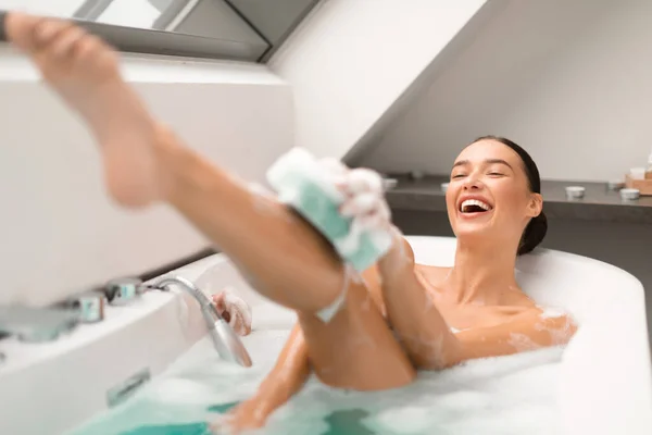 在家里的现代浴室里 快乐的女士洗浴用的是洗浴用的洗发水凝胶 通过海绵洗身体 女人喜欢用泡沫洗澡 健康与身体护理化妆品 选择性焦点 — 图库照片