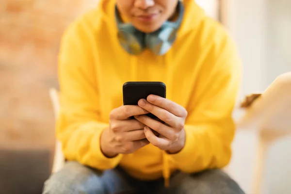 Cropped Shot Of Teenager Guy Using Smartphone Texting And Playing Mobile Games Sitting At Home. Selective Focus On Cellphone In Students Hands. Gadgets And Social Media Concept