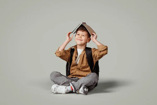 Sırt Çantalı Küçük Avrupalı Çocuğun Kitabı Kafasına Geçirip Yere Oturmasına — Stok fotoğraf