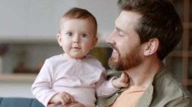 Baba-kız ilişkisi. Babasının elindeki sevimli küçük kızın yakın portresi kameraya gülümsüyor, babasını küçük kızını öpüyor, yavaş çekimde, takip çekiminde.