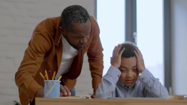 世代間のギャップ 怒り狂ったアフリカ系アメリカ人の父親彼の小さな息子を叱り 机の上に座って頭を抱え 父親の態度に苦しみ ゆっくりとした動き 自由な空間 — ストック動画