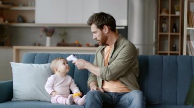 Hastalık belirtileri. Genç, endişeli bir baba, kızının vücut ısısını ölçüyor ve ateşi görüyor, oynak bir kızın alnına dokunuyor, yavaş çekim, serbest alan.