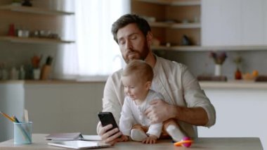 Sinir bozucu ebeveynlik. Genç, meşgul bir menajer, aktif bebek kızıyla bebek bakıcılığı yapıyor ve akıllı telefon üzerinde çalışmaya çalışıyor, gözlerini yuvarlıyor, kızı masada tutuyor, çekimleri takip ediyor, boş alan arıyor.