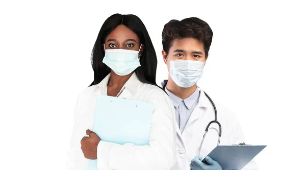 卫生保健概念 多民族医生头戴保护面罩站在白色背景之上 身穿制服的男女医务工作者拿着剪贴板 凝视着相机和胶合板 — 图库照片