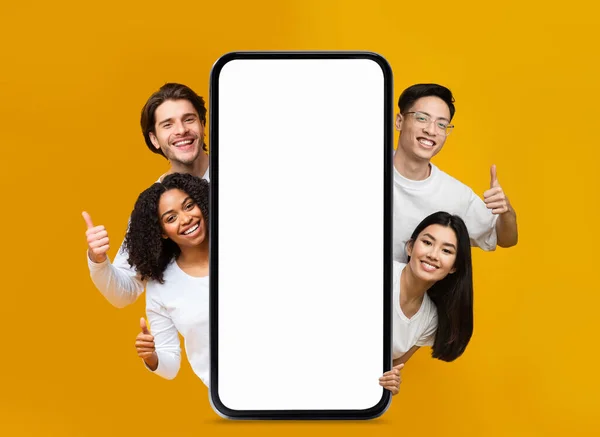 Diverse Happy People Peeking Out Behind Big Blank Smartphone And Showing Thumb Up Over Yellow Background, Multiethnic Men And Women Recommending Online Offer Or Mobile Advertisement, Collage, Mockup