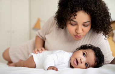 Afrikalı genç Amerikalı bayanı sevmek, çocukla kanepeye uzanmak, bebeği öpmek, aydınlık yatak odasının iç kısmının tadını çıkarmak. Aile sevgisi, anne ve çocuk evde, bebek bakımı.