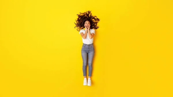 Wow Offer. Excited Woman Touching Face Looking At Camera In Excitement Posing Lying Over Yellow Studio Background, View From Above. Beauty And Fashion Concept. Full Length Shot, Panorama