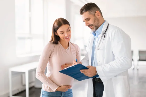 Mężczyzna Lekarz Pokazuje Schowek Wynikami Badań Medycznych Szczęśliwej Kobiety Ciąży — Zdjęcie stockowe