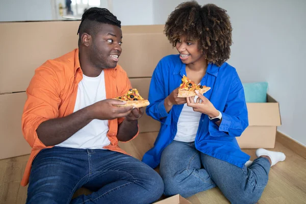 stock image Young Black Couple Eating Pizza And Relaxing On Floor On Moving Day, Romantic African American Spouses Sitting Among Cardboard Boxes, Taking Lunch And Celebrating Relocation, Closeup Shot