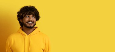 Heyecanlı, mutlu, kıvırcık, sarı kapüşonlu genç Hintli adam fotokopi odasına bakıyor ve sarı stüdyo geçmişine gülümsüyor.