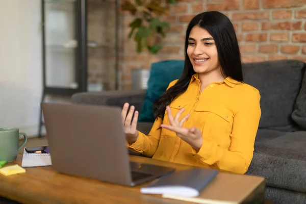Positive spanish lady having online lesson or making video call with laptop, talking and gesturing at camera, having teleconference, enjoying online communication at home