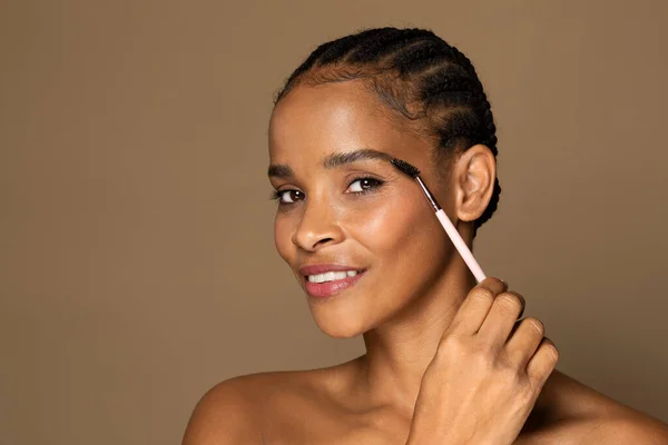 自然妆容迷人的中年黑人妇女手握画笔 微笑着擦拭眉毛 享受着日常的美感 棕色背景 自由自在的空间 女性化妆品产品 — 图库照片