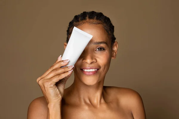 Szczęśliwa Czarna Kobieta Średnim Wieku Trzyma Tubę Kremem Kosmetycznym Pobliżu — Zdjęcie stockowe