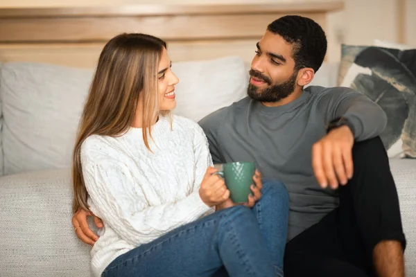 微笑的国际千禧年情侣拥抱坐在地板上 一起享受闲暇的时光和一杯咖啡 在简约的客厅里聊天 爱情和感情 在家里休息吧 — 图库照片