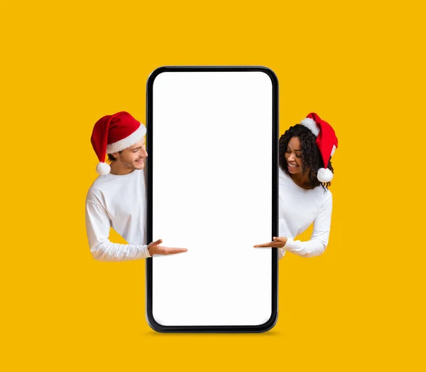圣诞大甩卖圣诞兔子中快乐的年轻夫妇在大块空白智能手机前指点 快乐的男人和女人在白屏前展示手机 展示广告 调侃的复制空间 — 图库照片