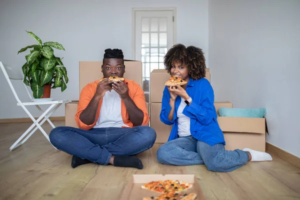 stock image Happy Black Couple Celebrating Moving Into New Home, Sitting On Floor And Eating Takeaway Pizza, Young African American Man And Woman Resting Among Cardboard Boxes, Enjoying Tasty Lunch, Free Space