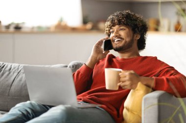 Mobil İletişim. Cep telefonuyla konuşan yakışıklı Hintli genç adam ve evde dizüstü bilgisayar kullanan, mutlu doğulu serbest çalışan, kahve içen ve cep telefonu sohbetinin keyfini çıkaran adam,