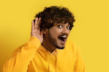 Heyecanlı, genç, neşeli, kıvırcık, kıvırcık, sarı kapüşonlu bir adam. Kulağının yanında el ele tutuşuyor ve sarı stüdyo geçmişine kulak misafiri oluyor. Heyecan verici haberler ve dedikodular dinliyor.