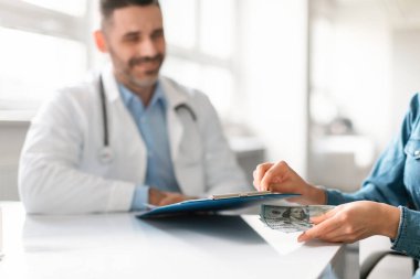 Kadın hasta doktor panosunun altına para koyuyor, klinikteki masada oturuyor, adam ona bakıyor ve gülümsüyor. Sağlık, ilaç, rüşvet ve suç